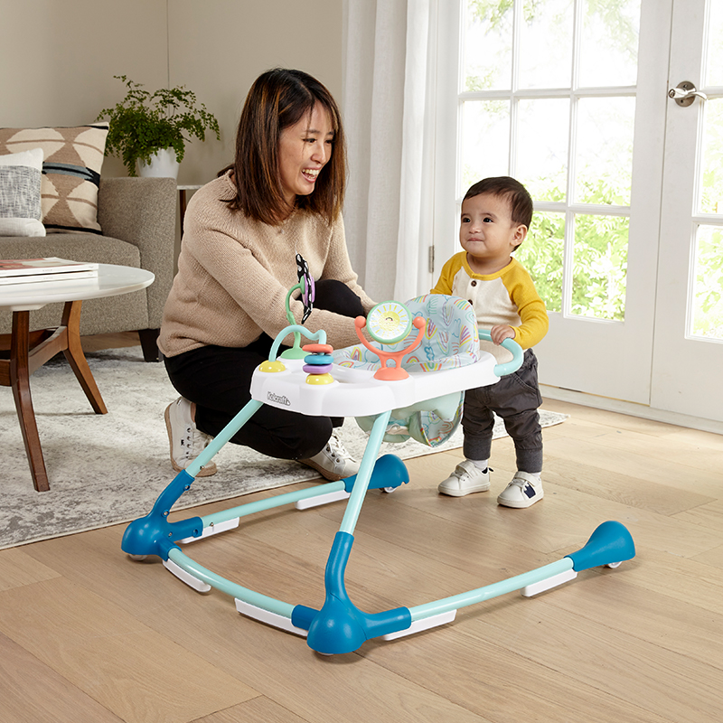 Infant standing behind the Kolcraft walker with mom